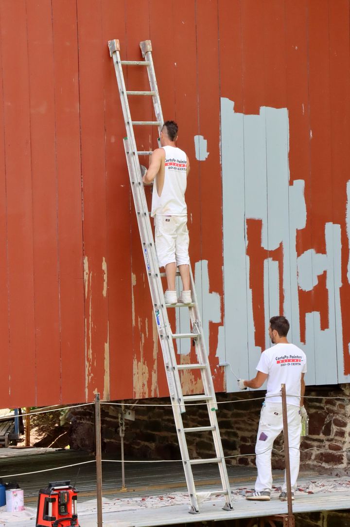 Two painters repainting a tall exterior wall from a ladder