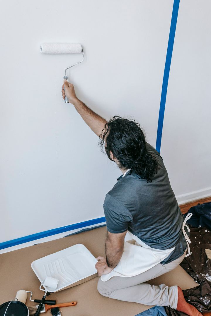 Painter rolling fresh paint on a wall with taped edges